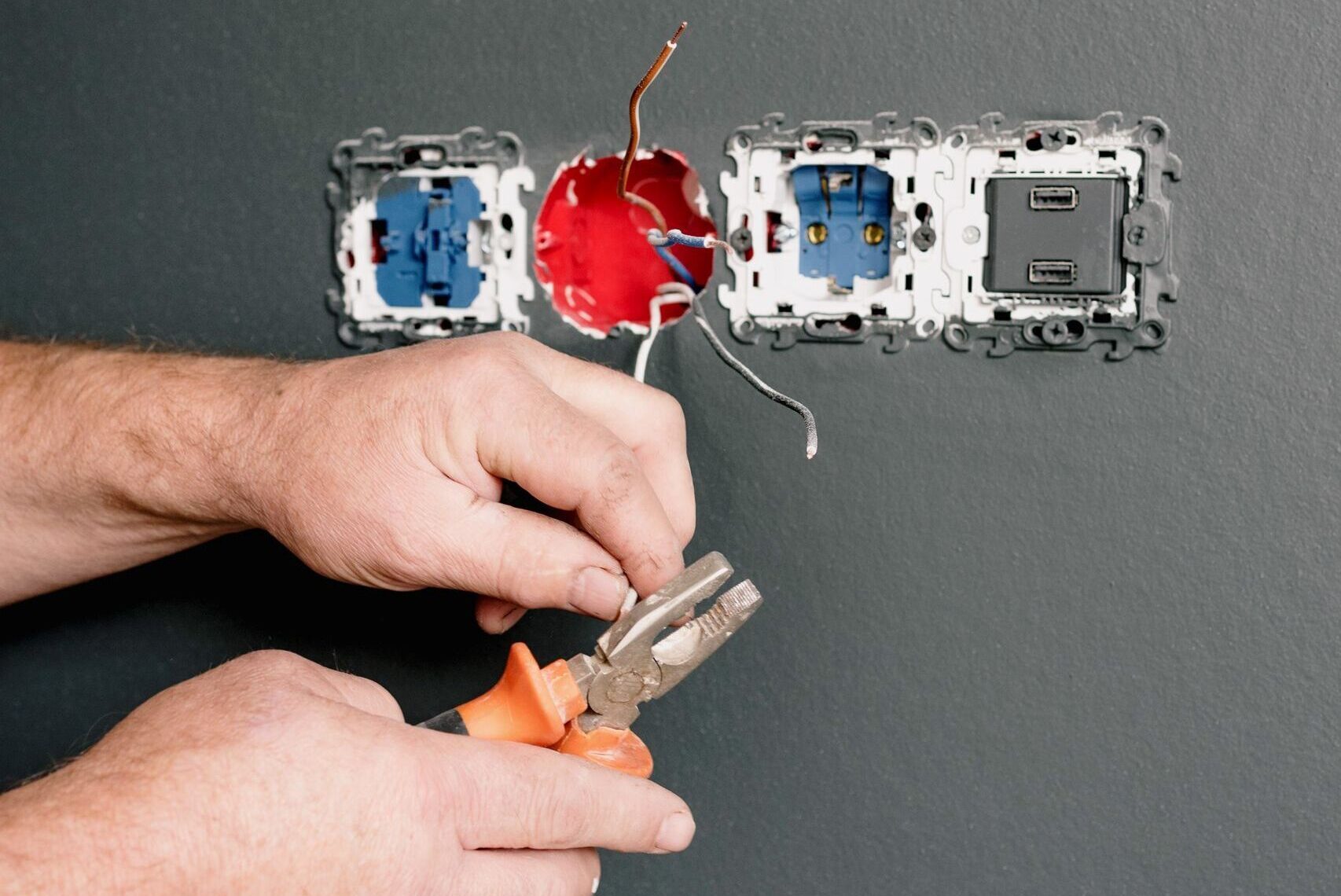 Crop faceless electrician using pliers for installation sockets and switches in new apartment